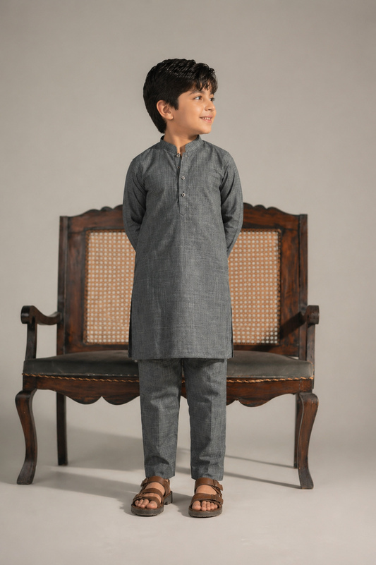 Young boy in a gray kurta standing next to an ornate wooden chair