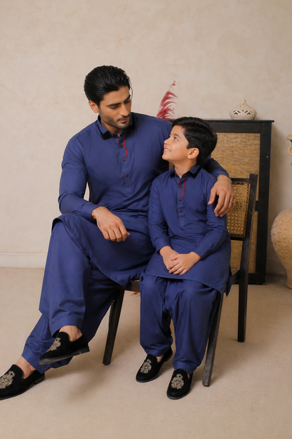 FATHER and child in matching blue outfits sitting on a chair against a beige wall.