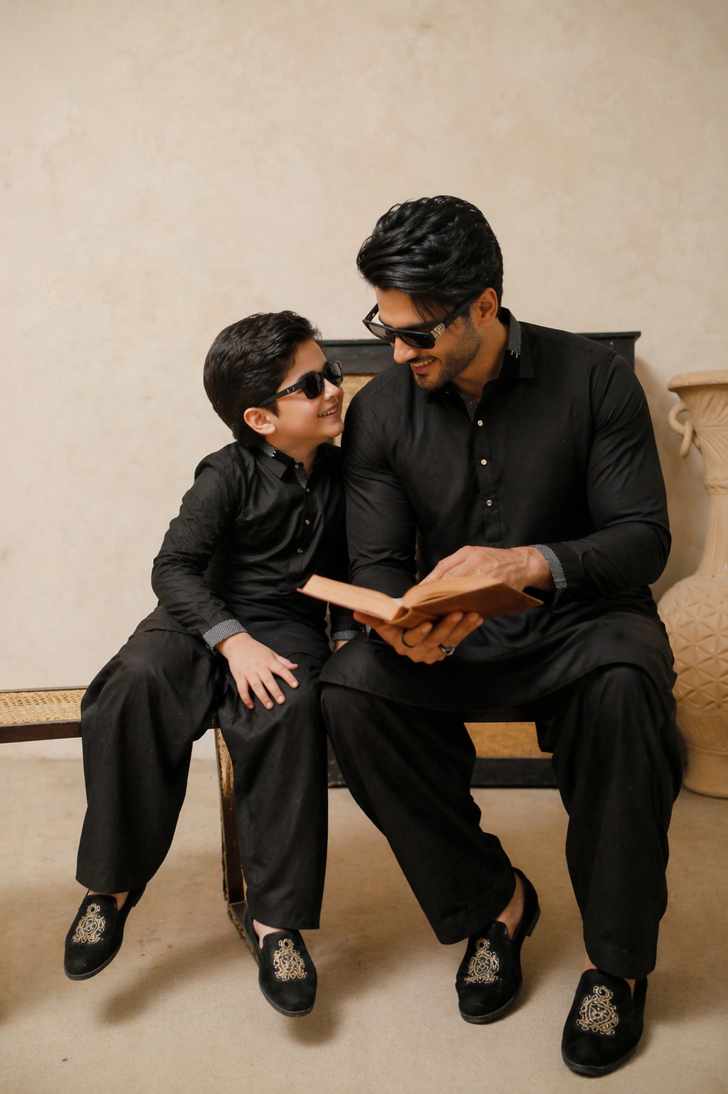 Father & Son in black outfits sitting together, reading a book.