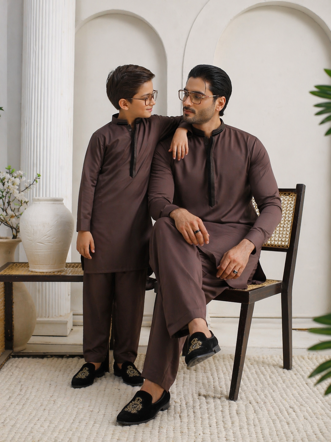 Father and young boy in matching brown outfits sitting together in a room with decorative elements.