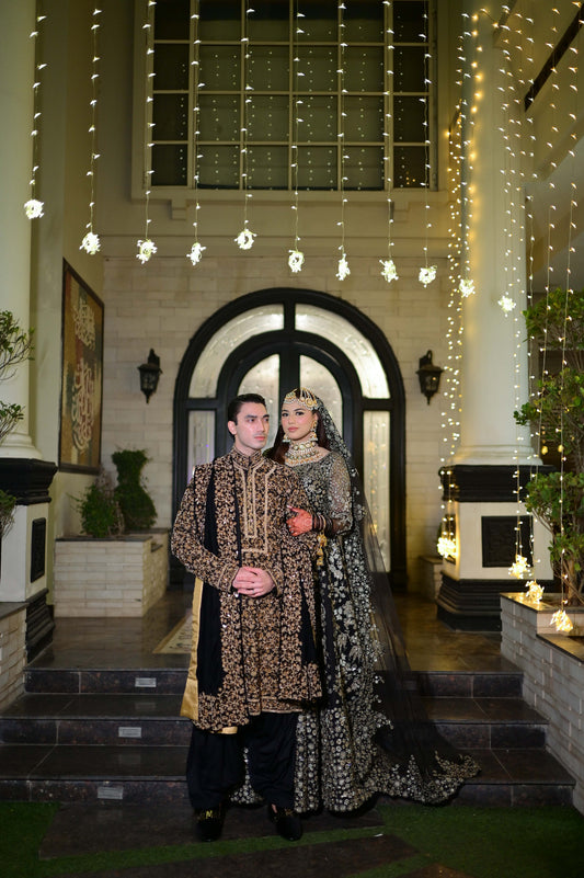 Two people in traditional attire standing in a decorated indoor setting with string lights.