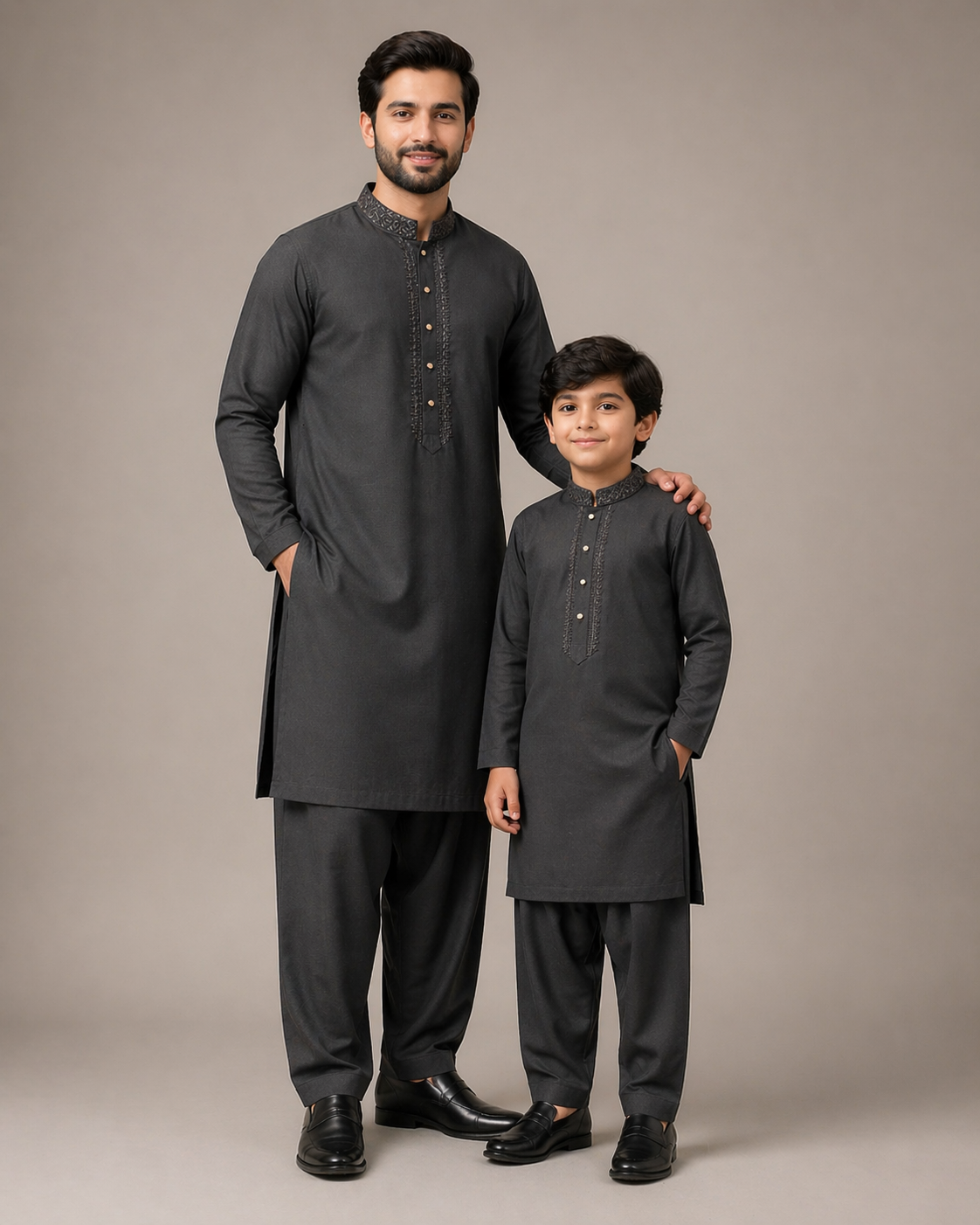 Man and child wearing matching black traditional outfits against a neutral background
