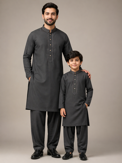 Man and child wearing matching dark gray traditional outfits against a neutral background
