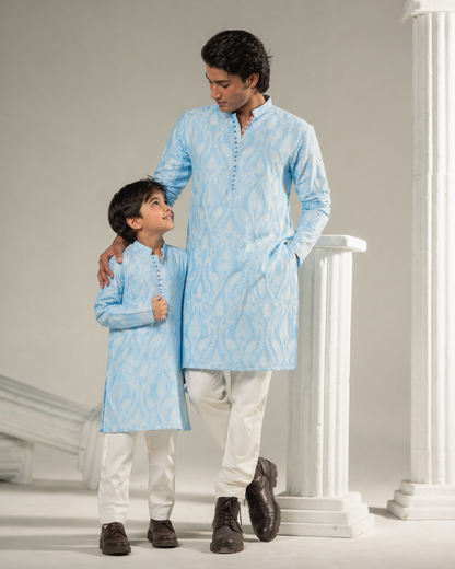 Man and child wearing matching light blue kurta sets on a white background
