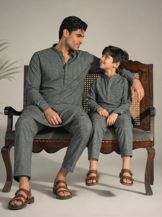 Man and child sitting on a wooden chair wearing matching gray outfits.
