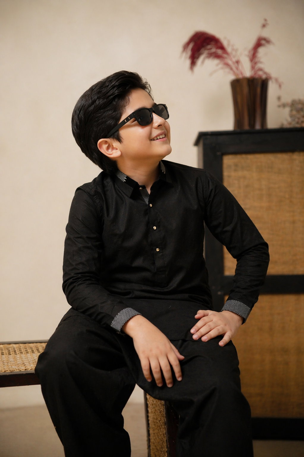 Young boy in a black outfit sitting on a chair with a neutral background