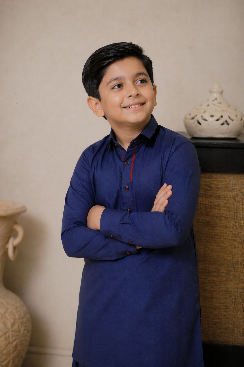 Young boy in a blue kurta standing indoors with decorative vases in the background