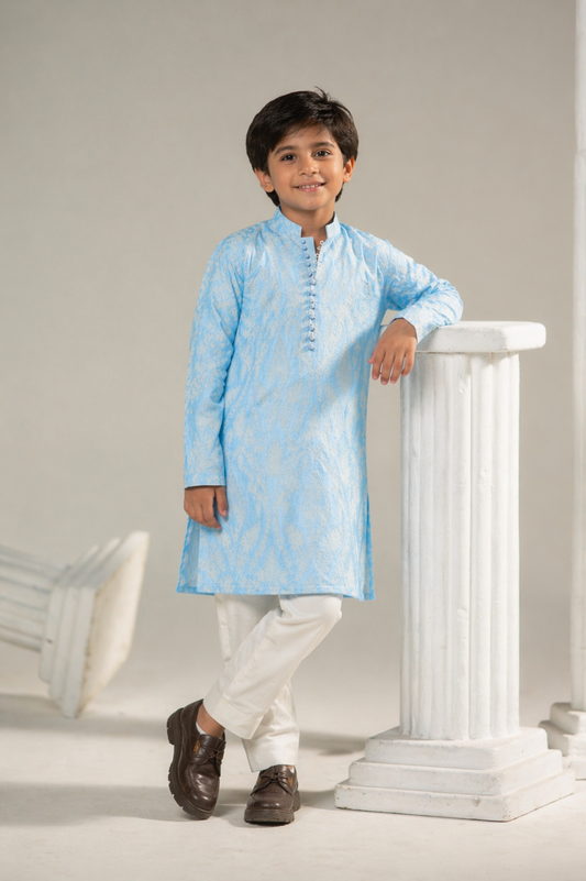 Young boy in a light blue kurta with white pants standing against a neutral background