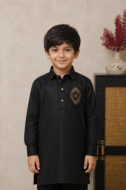 Young boy wearing a black kurta with a logo on a beige wall.