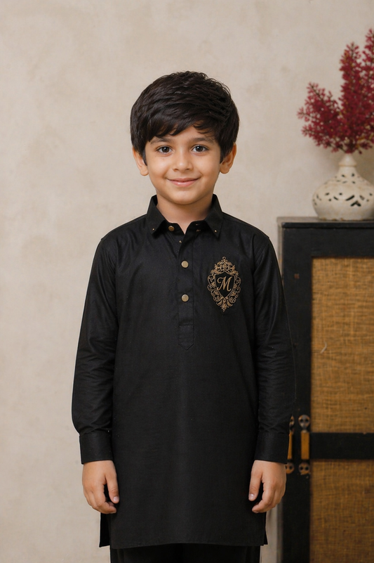 Young boy wearing a black kurta with a logo on a beige wall.