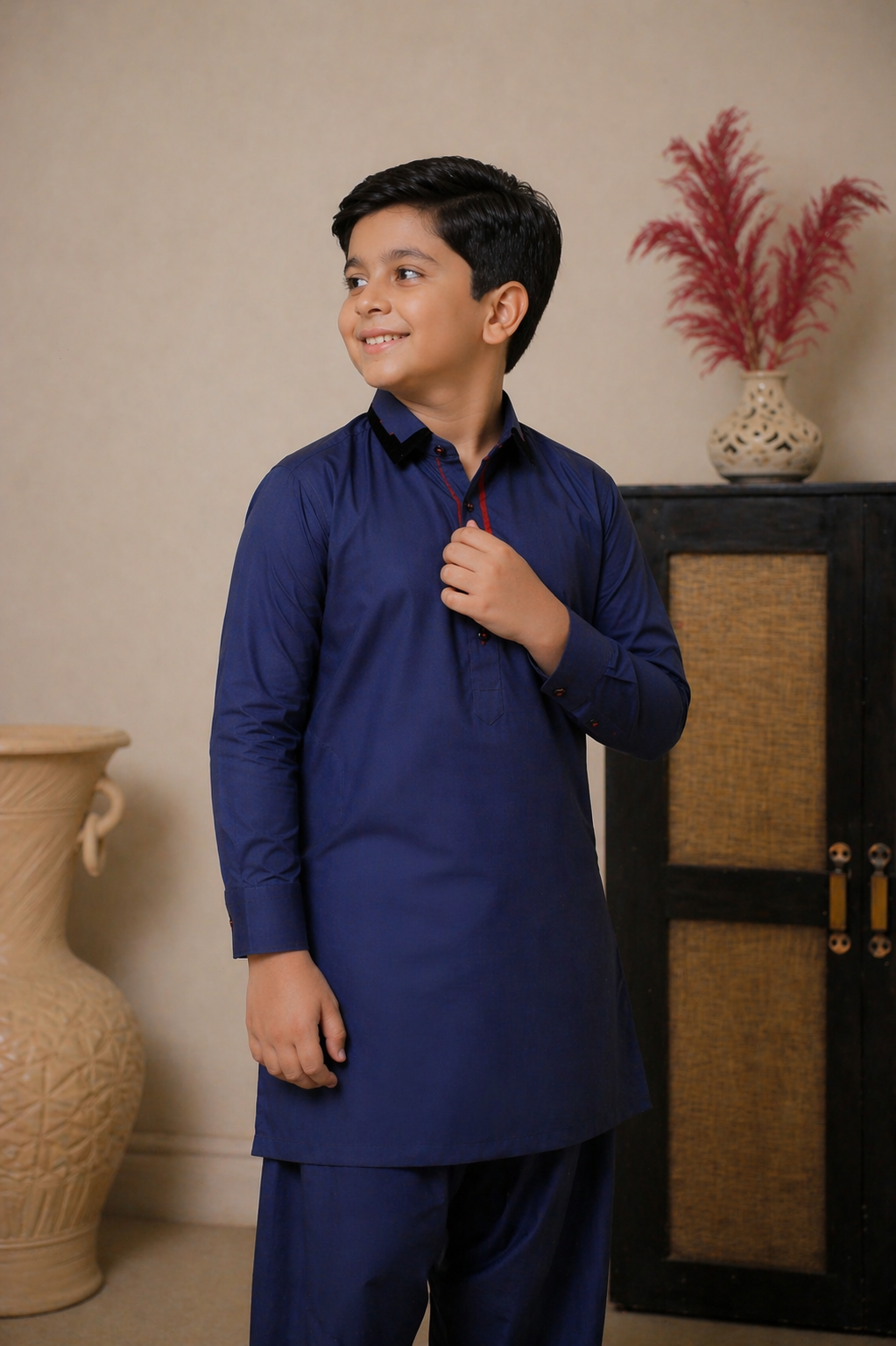 Young boy in a blue kurta standing indoors with decorative vases in the background