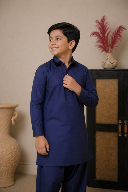 Young boy in a blue kurta standing indoors with decorative vases in the background
