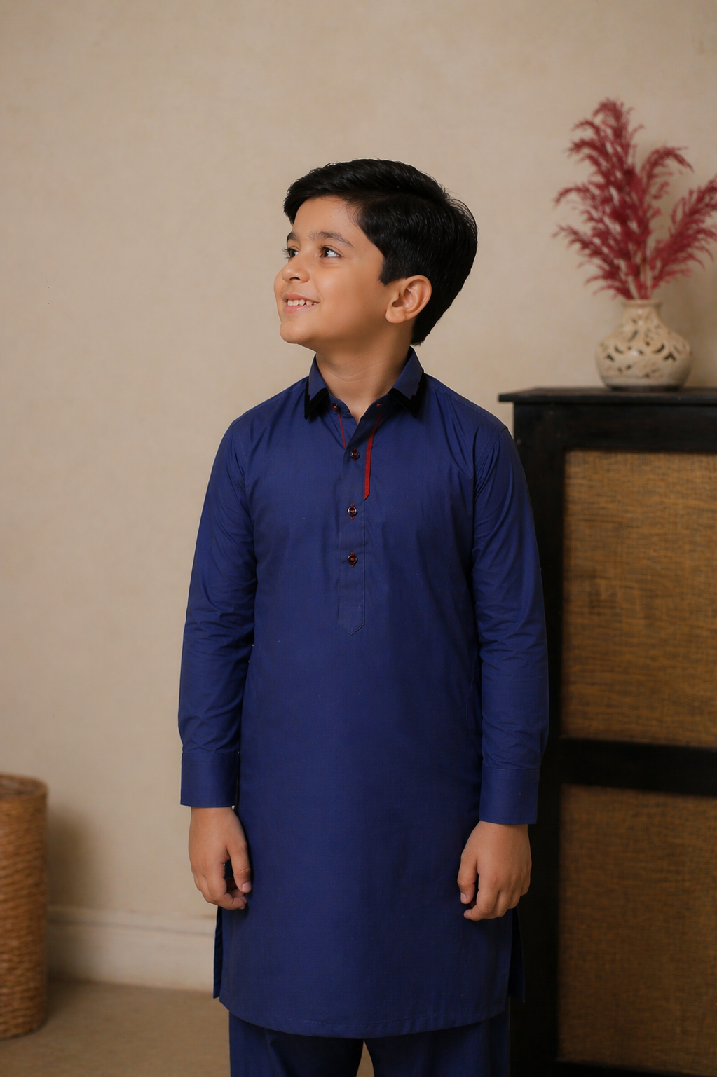 Young boy wearing a blue kurta standing indoors with a neutral background