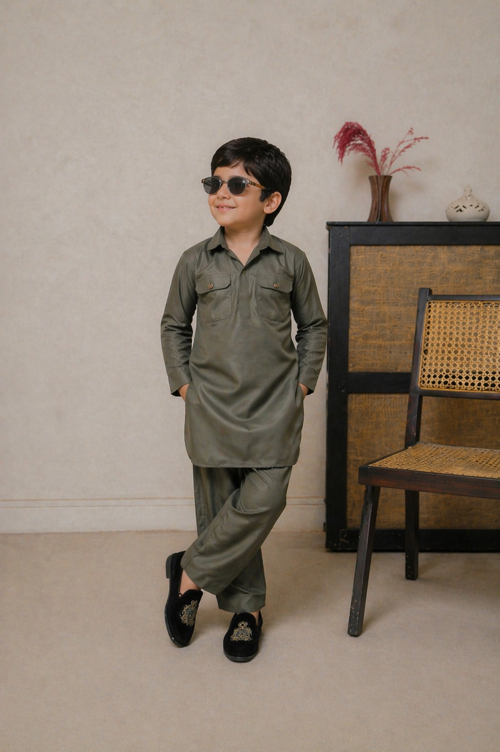 Child wearing a green outfit standing in a room with a chair and decorative items.